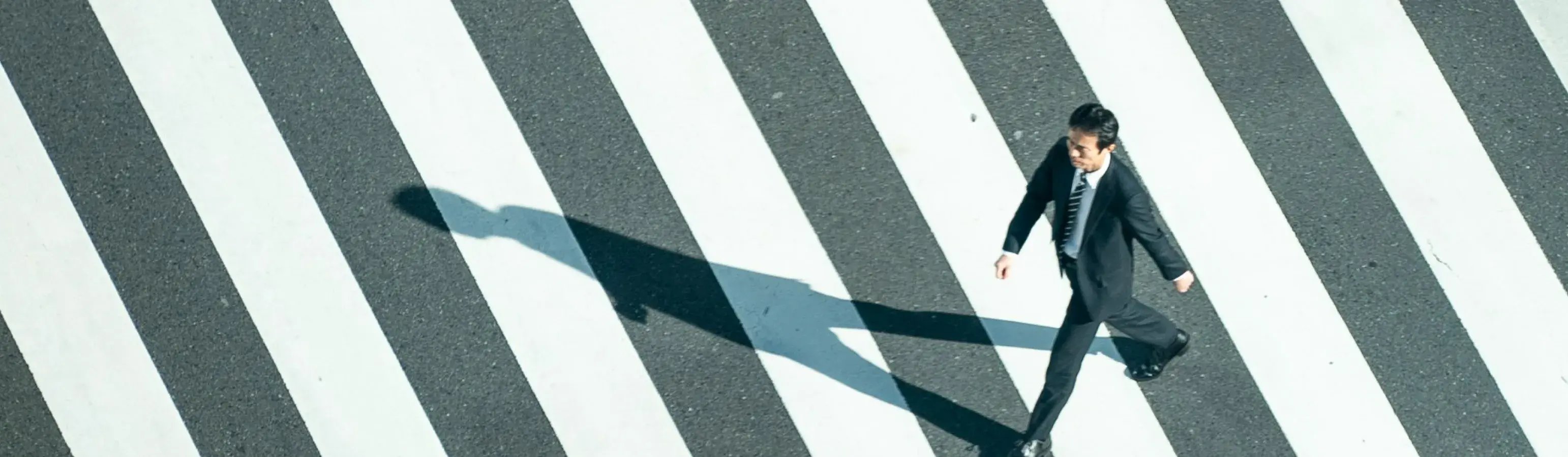 横断歩道を歩くスーツ姿のビジネスマンを真上から捉えた俯瞰写真_メインビジュアル_pc