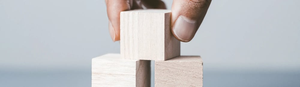 2つの木製ブロックの間に、3つ目のブロックを慎重に積み上げている手元のクローズアップ_メインビジュアル_pc